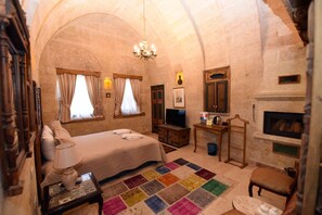 A bedroom with a bed, a television, a desk, a chair, a fireplace, and a colorful rug.