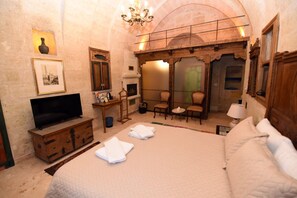 A hotel room with a bed, a television, a fireplace, and a seating area with chairs and a table. - 1860 KADIEVİ (Ürgüp)