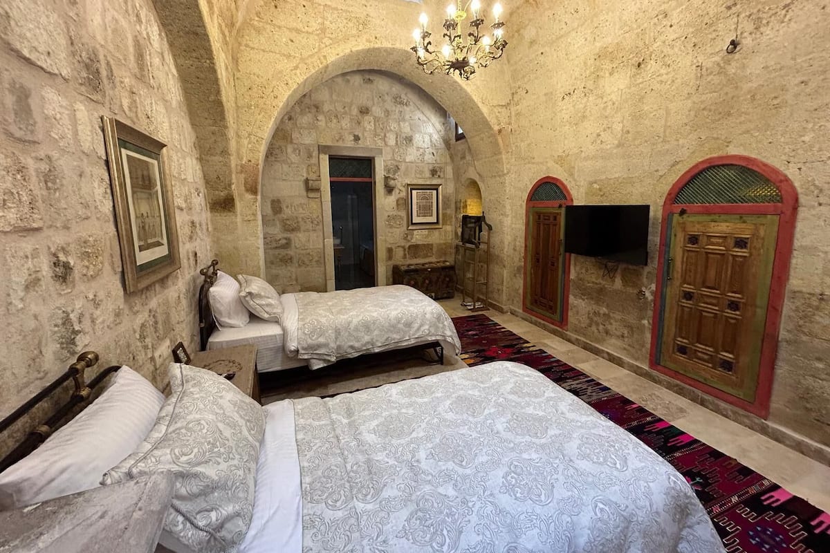 A room with two beds, a chandelier, and arched stone walls.