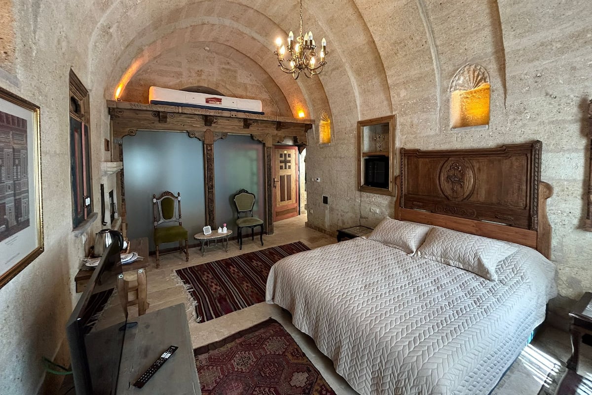A bedroom with a large bed, a chandelier, and a stone archway.