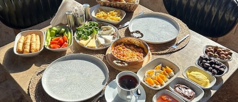 A breakfast table with various dishes, including fruits, cheeses, and bread, set in a sunny room with a view of a snowy landscape.
