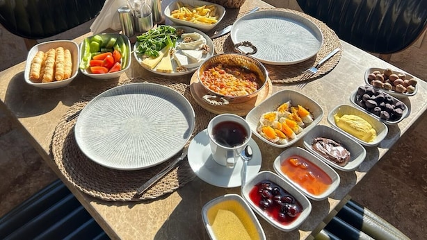 A breakfast table with various dishes, including fruits, cheeses, and bread, set in a sunny room with a view of a snowy landscape.