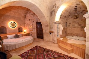 A room with a bed, a wooden bench, a bathtub, and a patterned rug. - 1860 KADIEVİ (Ürgüp)