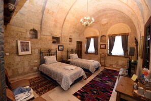 A room with two beds, a chandelier, and a patterned rug.