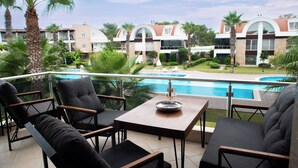 Ein Balkon mit Sitzgelegenheit im Freien, einem Pool und Blick auf Hotelgebäude.
