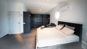 Ein modernes Schlafzimmer mit einem großen Bett, einem begehbaren Kleiderschrank und einem runden Spiegel an der Wand.