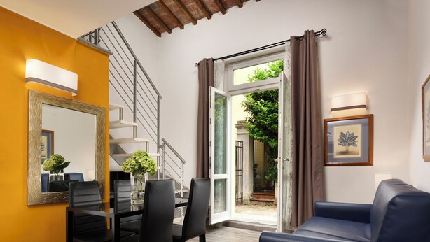 A dining area with a table and chairs, a staircase, and a view through an open door to a garden. - FH55 Med Guesthouse (Florence)