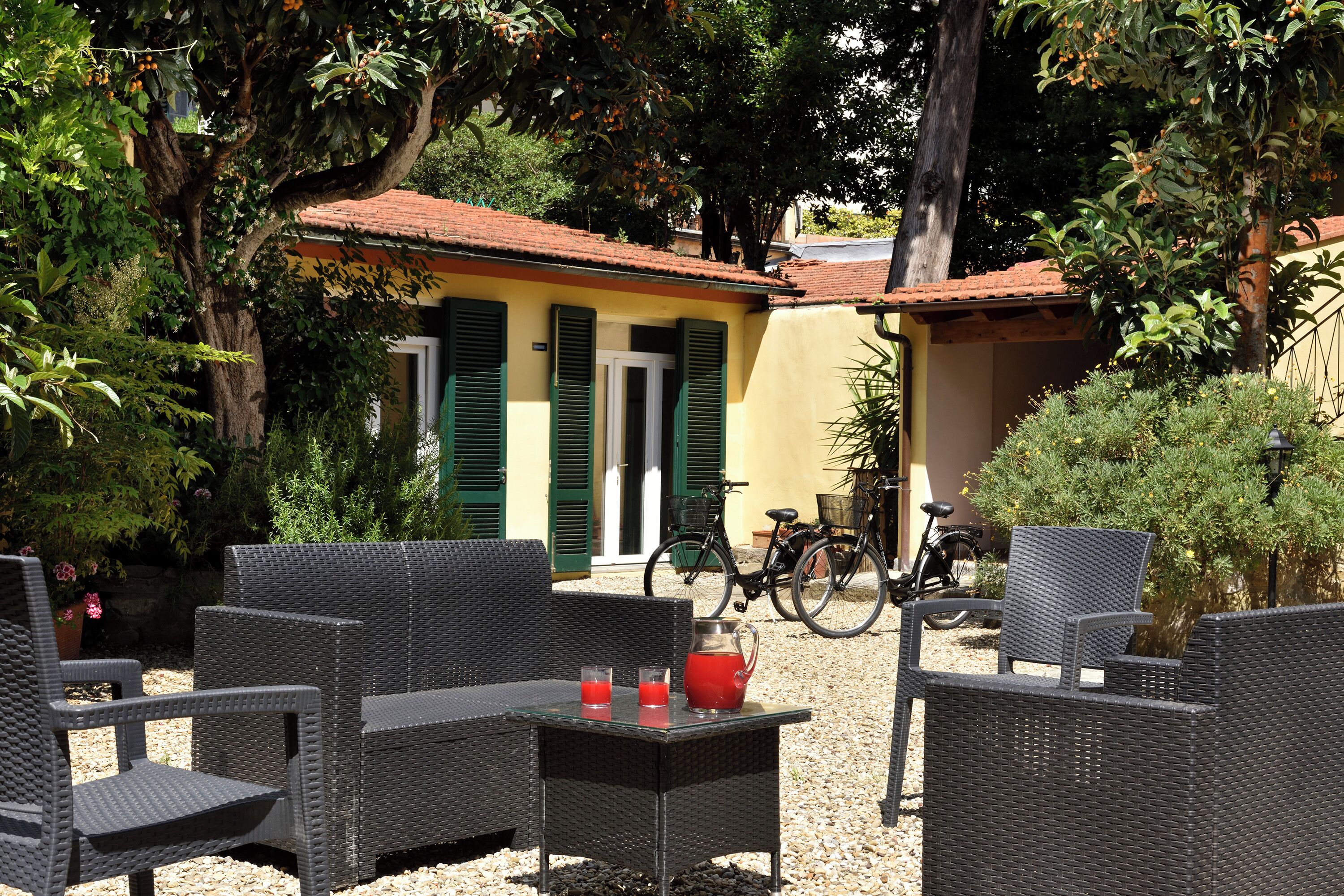 Un espacio al aire libre con mobiliario de mimbre, una mesa con bebidas y bicicletas estacionadas cerca.