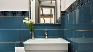 A bathroom with a white sink, blue tiles, a window, and a vase with flowers. - FH55 Med Guesthouse (Florence)