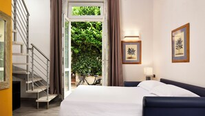 A hotel room with a bed, a desk, a chair, a staircase, and a view of greenery outside. - FH55 Med Guesthouse (Florence)