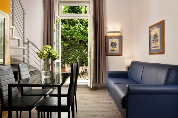 Una sala de estar moderna con un sofá azul, una mesa de comedor con sillas y una escalera.