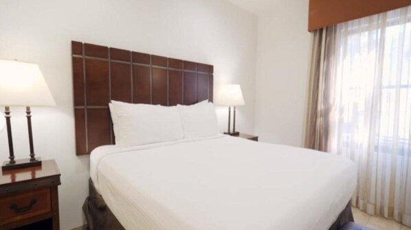 Habitación de hotel con una cama grande, dos mesitas de noche con lámparas y un ventanal con cortinas.