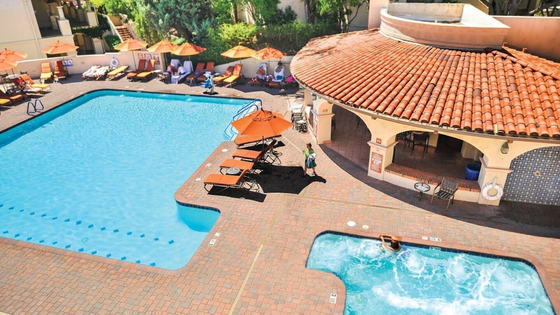 Ein großer Außenpool mit Liegestühlen und Sonnenschirmen, ein kleinerer Whirlpool und eine überdachte Terrasse.