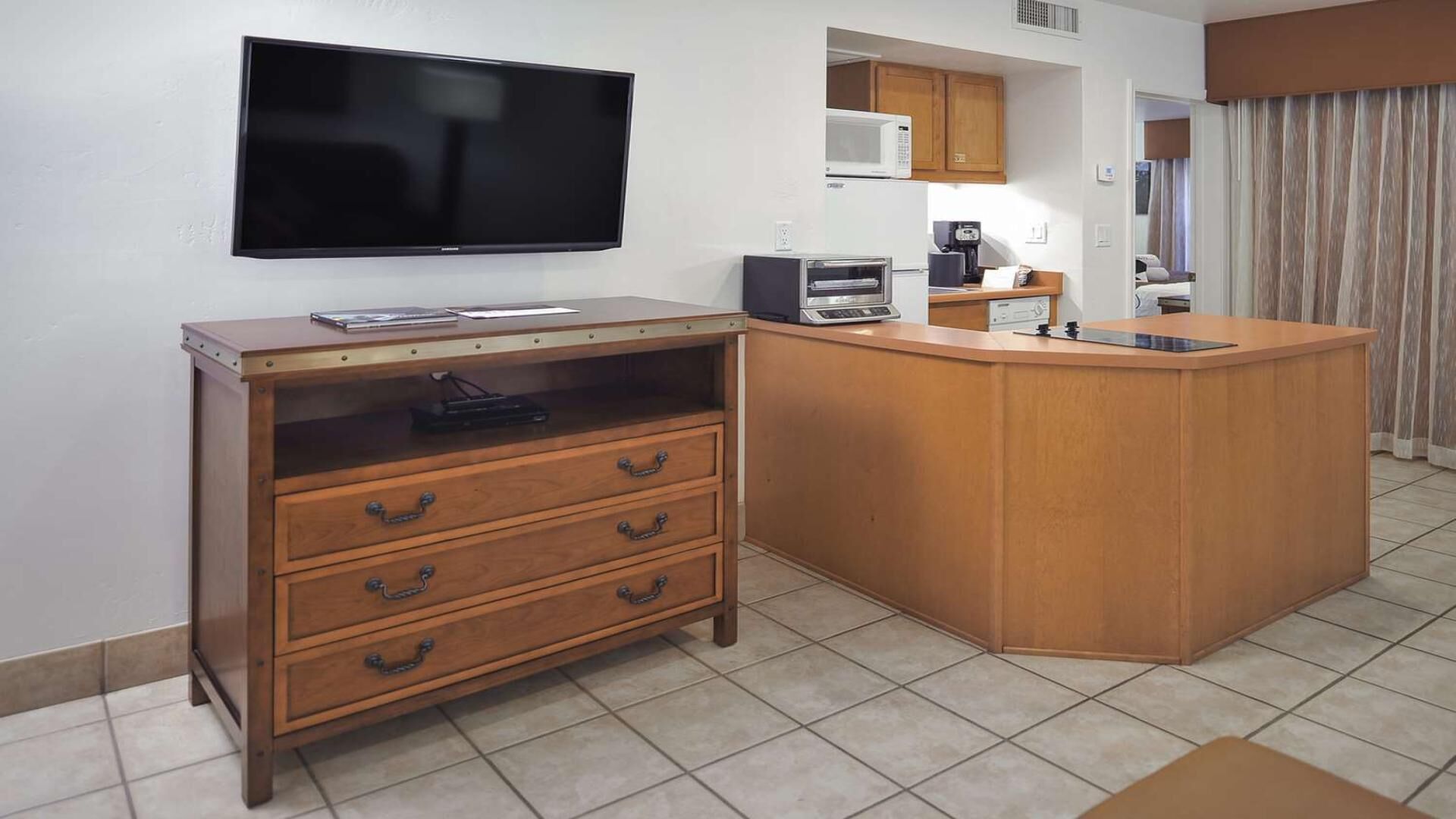 A compact kitchen with a flat-screen TV, wooden cabinetry, a coffee maker, and a microwave.