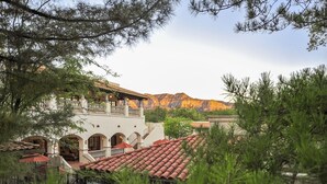 A building with a red-tiled roof, arched windows, and a balcony overlooking a mountainous landscape.