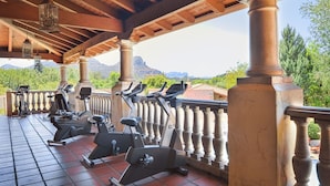 A covered outdoor area with exercise equipment, columns, and a view of mountains.