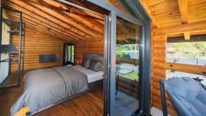 A modern log cabin bedroom with a large bed, a glass sliding door to a balcony, and a wooden ceiling.