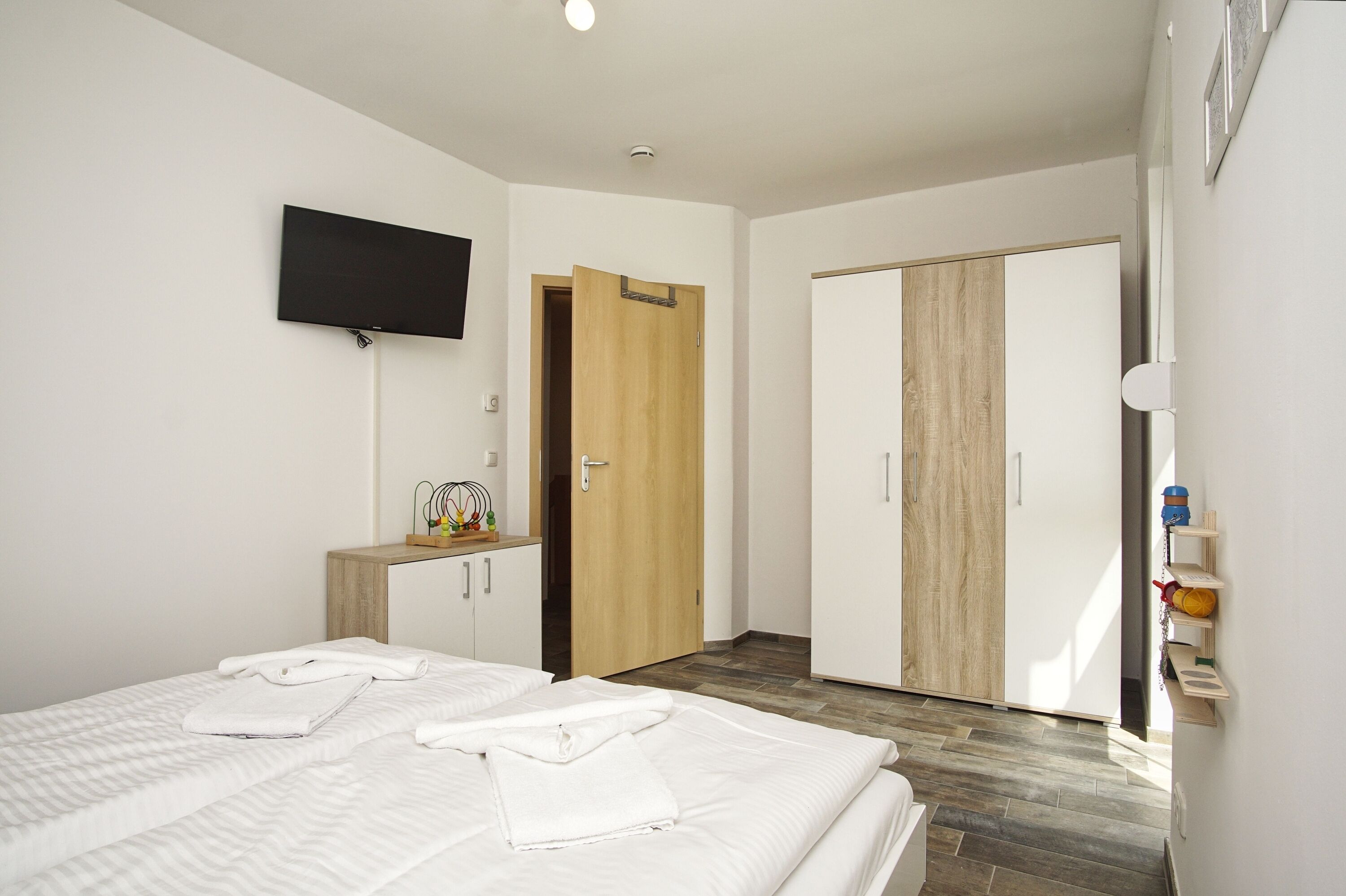 Ein Hotelzimmer mit Bett, Wandfernseher, Kleiderschrank und kleinem Schreibtisch mit Stuhl.