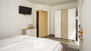 Habitación de hotel con cama, televisor montado en la pared, armario y un pequeño escritorio con silla.