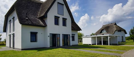 A modern house with a thatched roof, a covered outdoor seating area, and a well-maintained lawn.