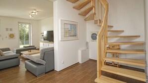 Una sala de estar moderna con una escalera de madera, sofás grises, una mesa de centro y un televisor.