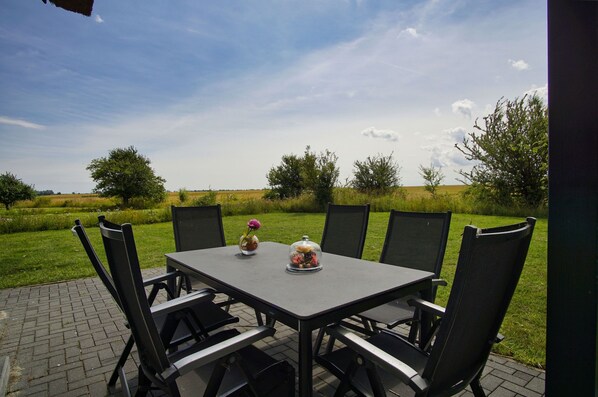 Eine Terrassengruppe im Freien mit Tisch, Stühlen, einer Blumenvase und einem Dekorationsobjekt auf dem Tisch.