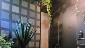 Une pièce avec un plancher en bois, une plante en pot, un mur noir avec une fenêtre et une petite étagère sur laquelle sont posés divers objets.