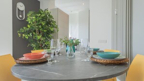 A round dining table with a clock on the wall, surrounded by yellow chairs, and a potted plant. - Como Panorama in Como (Como)