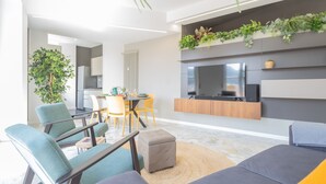 A modern living room with a sofa, chairs, a coffee table, a TV, and a kitchen area in the background. - Como Panorama in Como (Como)
