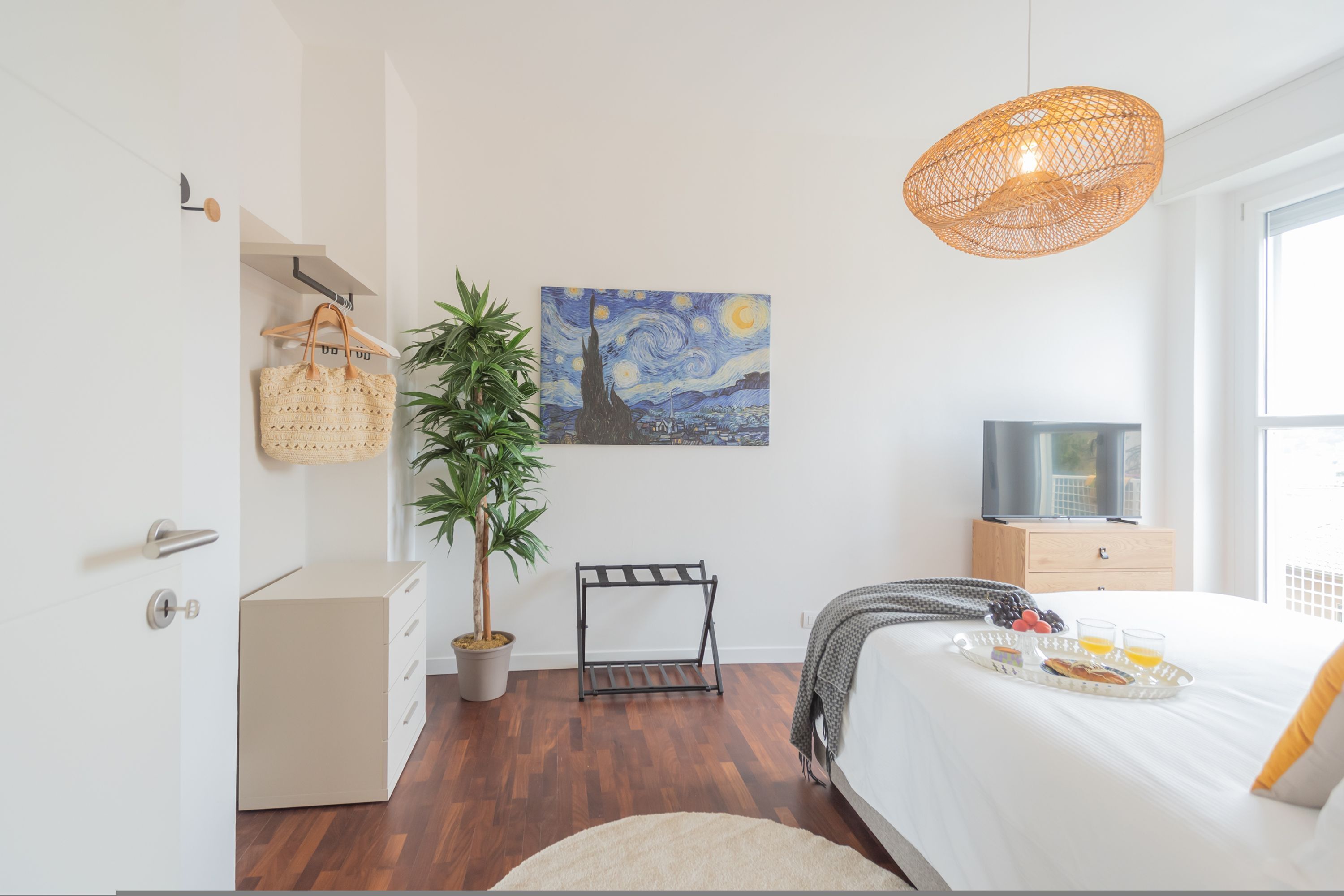 A modern bedroom with a bed, a painting, a hanging light, a plant, and a tray with breakfast.