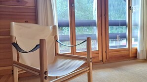 Une chaise en bois avec un coussin blanc, dans une pièce aux murs en bois et aux grandes fenêtres.