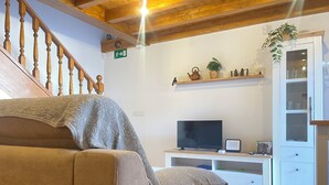 A cozy living room with a sofa, a television, a white cabinet, and a staircase. - Charming rural house Casa Zalo for 2-4 people in Mestas de Con (Cangas de Onís)