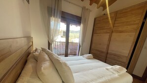 A bedroom with a wooden headboard, a neatly made bed with white linens, a balcony with a view, and a wooden wardrobe. - Charming rural house Casa Zalo for 2-4 people in Mestas de Con (Cangas de Onís)