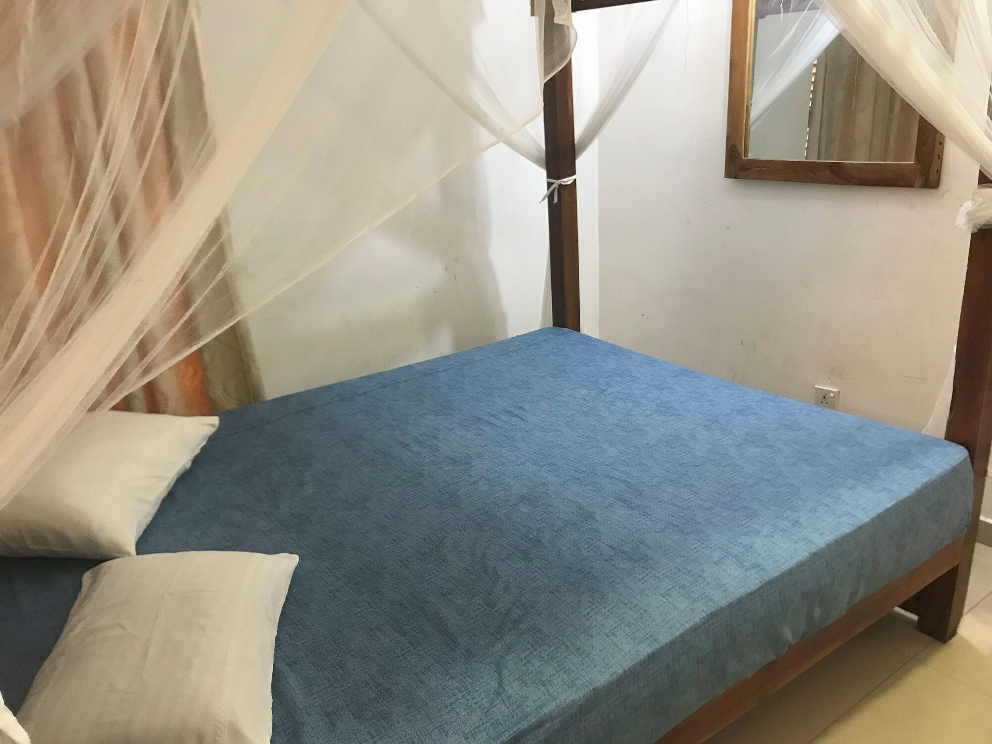 A single bed with a blue mattress and white pillows, a wooden headboard, and a mosquito net.