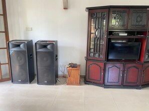 A room with two large speakers, a wooden cabinet with a television, and a door with a glass panel. - Stadium Reach Laythraa   (Kengalla)
