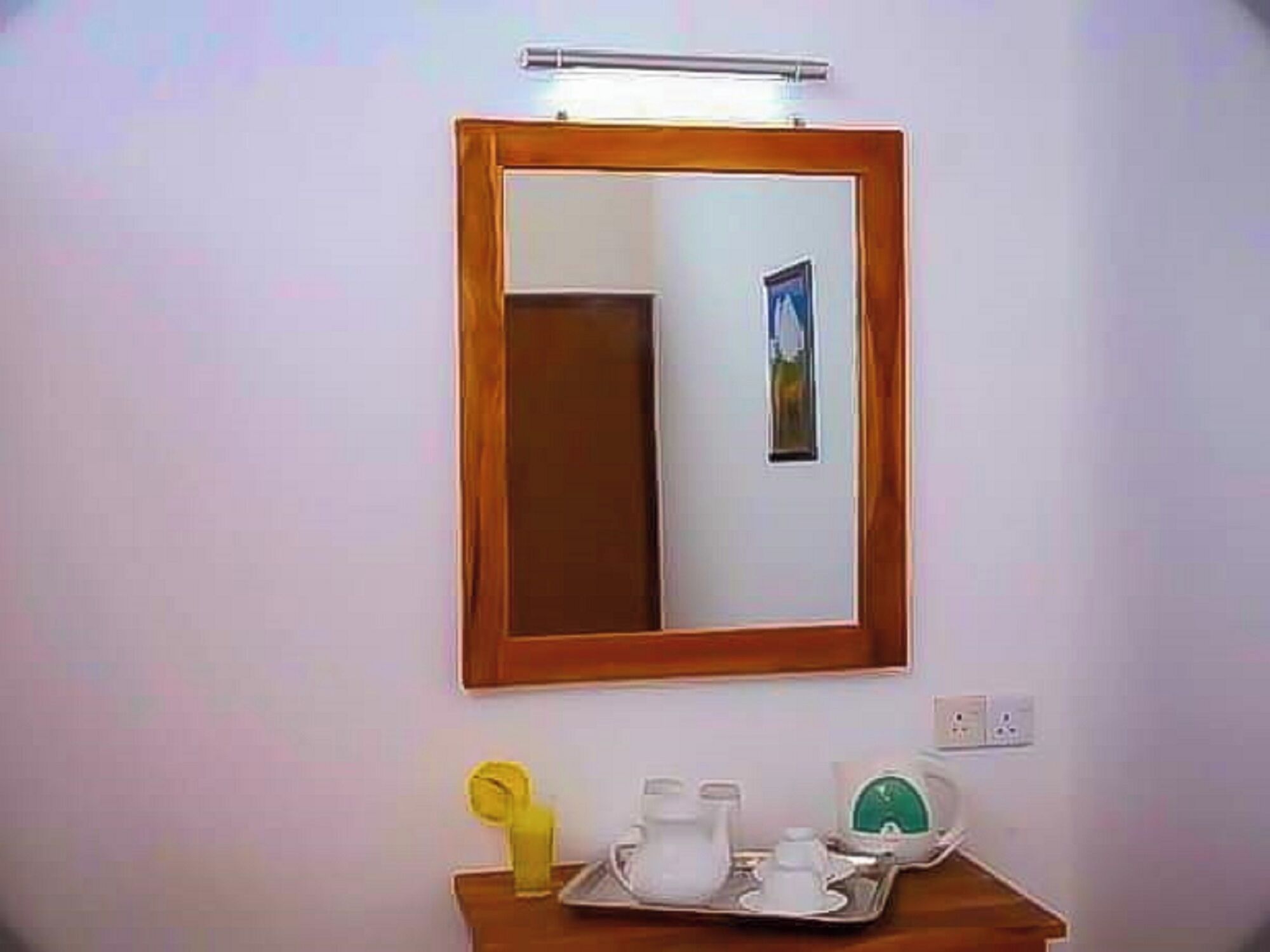 Une salle de bain avec un miroir encadré en bois, un lavabo avec des articles de toilette et un petit tableau accroché au mur.
