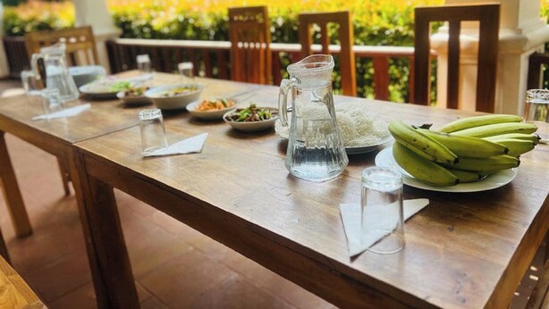 A wooden dining table with plates of food, a pitcher, and a bunch of bananas.