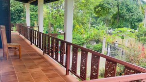 A covered balcony with a tiled floor and ornate railings, overlooking a lush garden.
