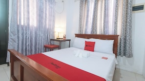 Una habitación de hotel con una cama de madera, una colcha roja y un almohadón con un logotipo rojo.
