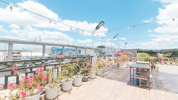 Une terrasse sur le toit, agrémentée de plantes en pot, d’une table et de chaises, d’où l’on peut admirer un panorama urbain avec un pont et des bâtiments.
