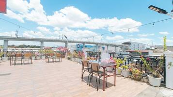 Una terraza en la azotea con varias mesas y sillas, rodeada de plantas y flores en macetas.