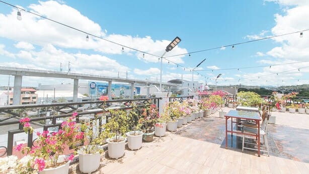 A rooftop terrace with potted plants, a table, and chairs, overlooking a cityscape with a bridge and buildings. - Reddoorz Near Lrt 2 Antipolo Station (Antipolo)