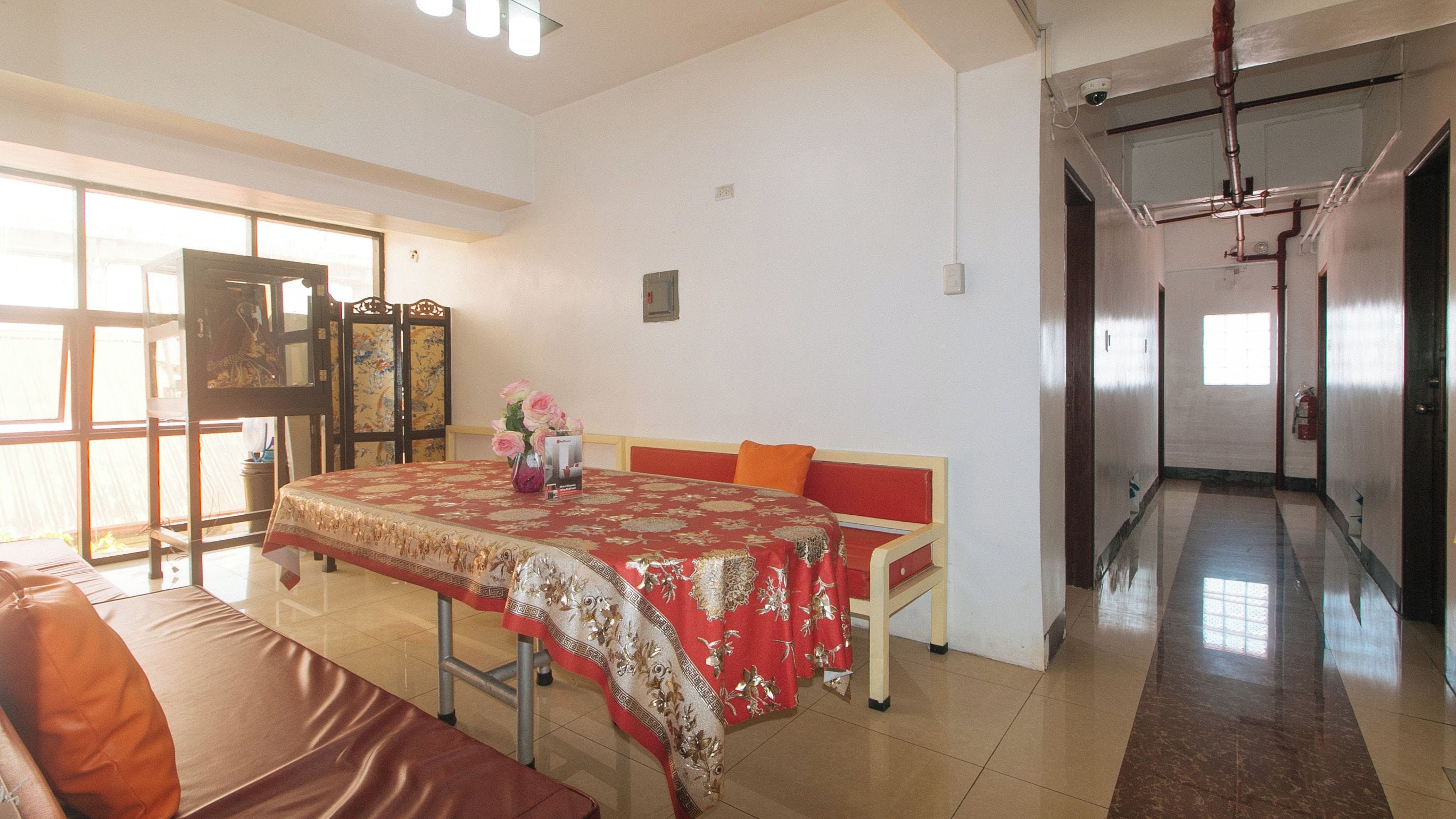 A hotel room with a large bed, a dining table with a red tablecloth, a sofa, and a view of the hallway.