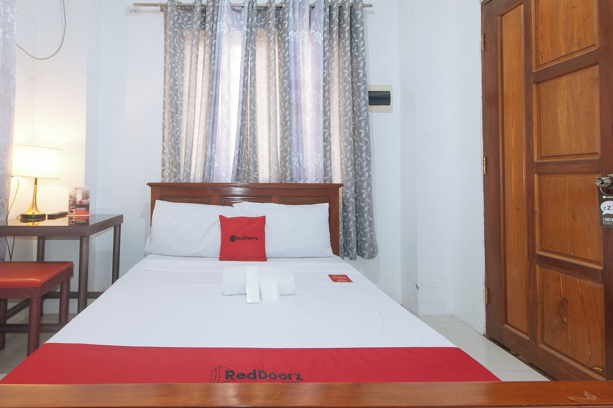 A hotel room with a bed, a nightstand, a lamp, and a door.