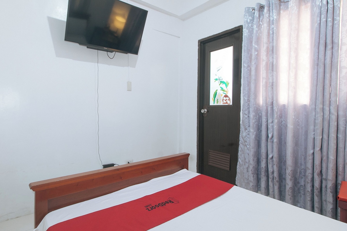 Ein Hotelzimmer mit einem Bett, einem an der Wand montierten Fernseher, einer Tür mit Fenster und einem Vorhang.