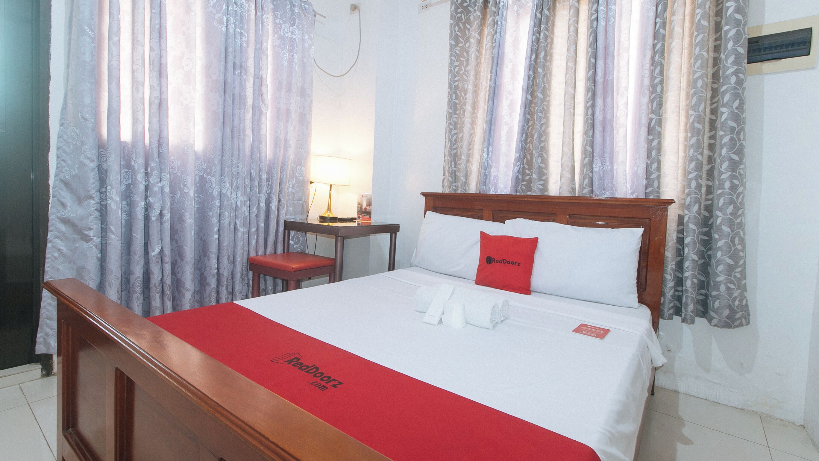 Une chambre d’hôtel avec un lit en bois, une couverture rouge et un oreiller orné d’un logo rouge.
