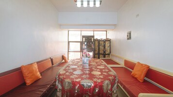 Una habitación con una mesa grande cubierta por un mantel estampado, rodeada de bancos con cojines rojos.
