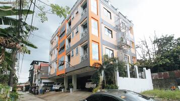 Un edificio residencial de varios pisos con balcones, estacionamiento techado y entrada protegida por un portón.