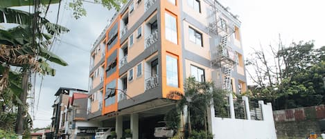 A multi-story residential building with balconies, a covered parking area, and a gated entrance.