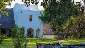 A white building with arched windows and a thatched-roof structure nearby. - Amani Beach Resort  (Kutani)